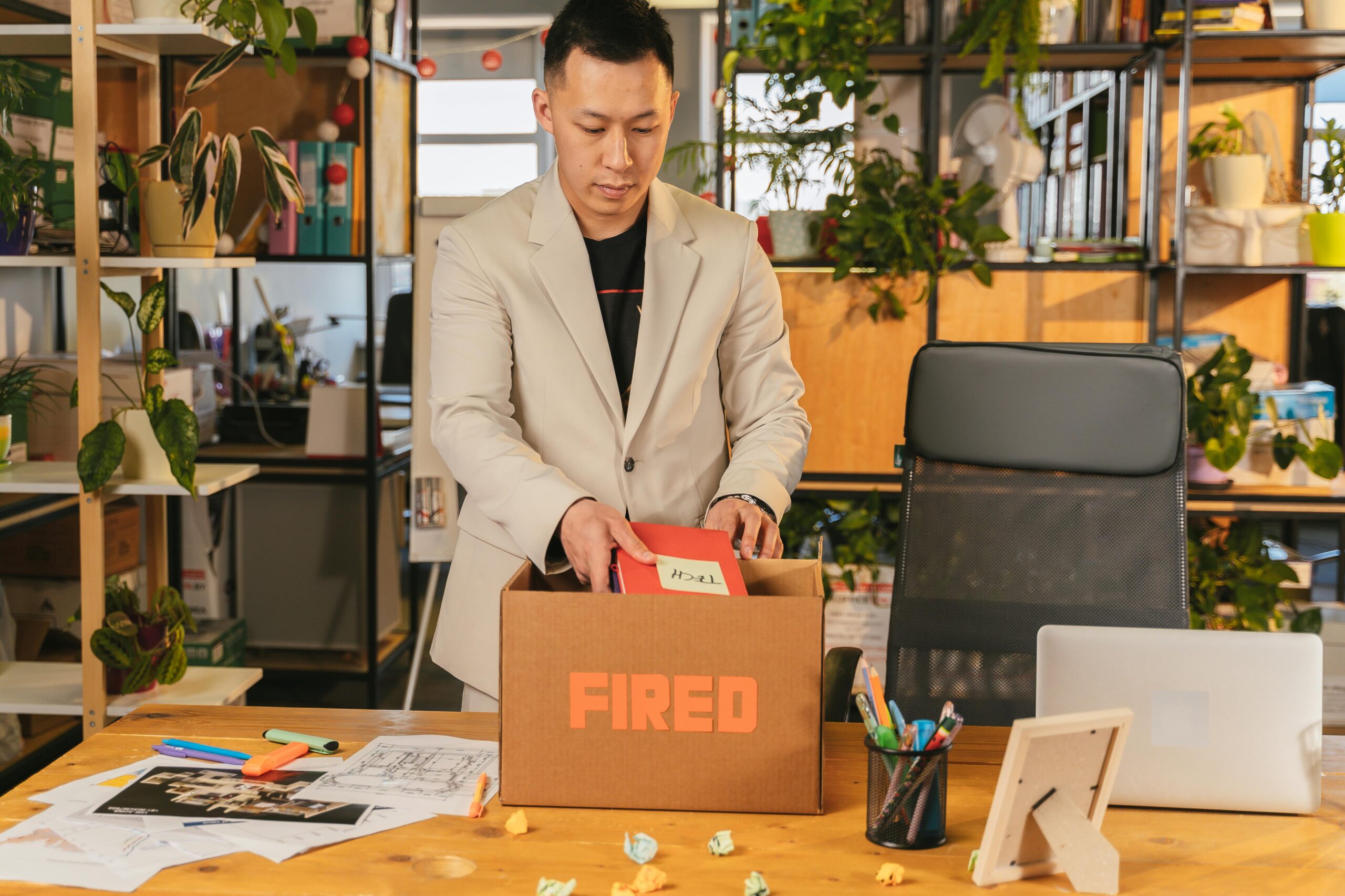 An adult man pack personal items after receiving a fired notice in an office setting, expressing corporate life challenges.